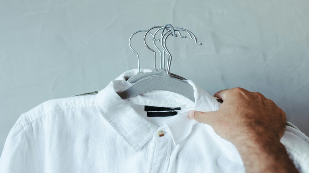 A man holding multiple white dress shirts.