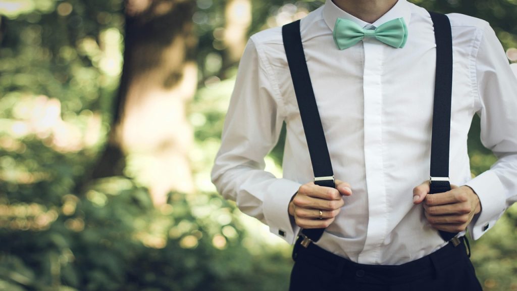 A man wearing a white long-sleeved shirt, a mint green bowtie, and black suspenders.