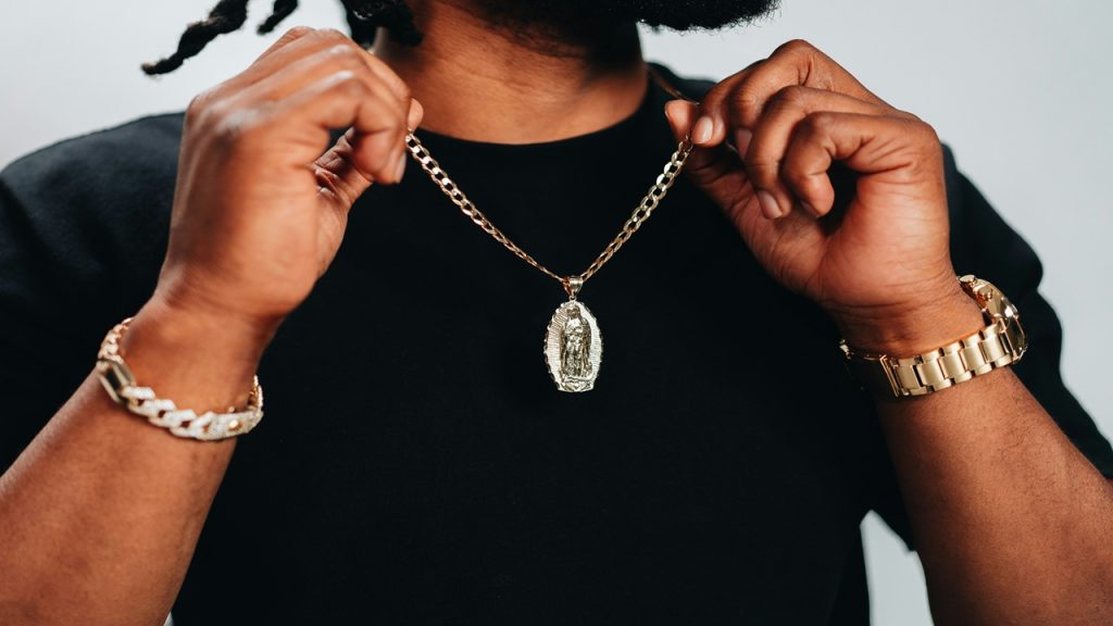 A man wearing a black shirt and a gold necklace, watch, and bracelet.
