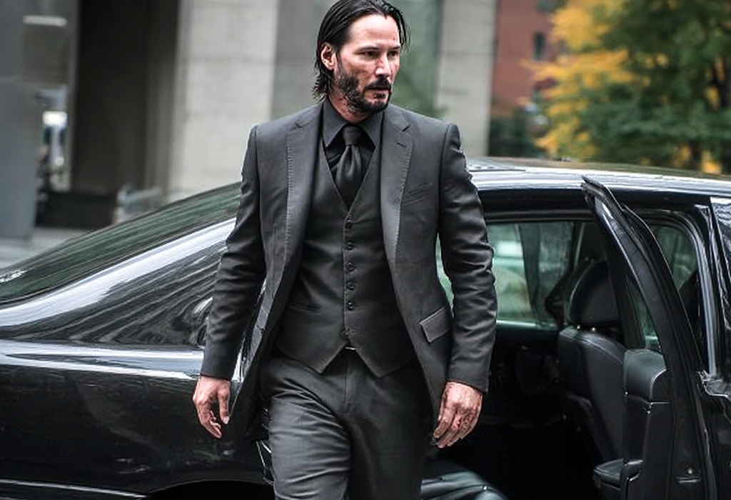John Wick wearing three-piece black suit stepping out of car, ready for action