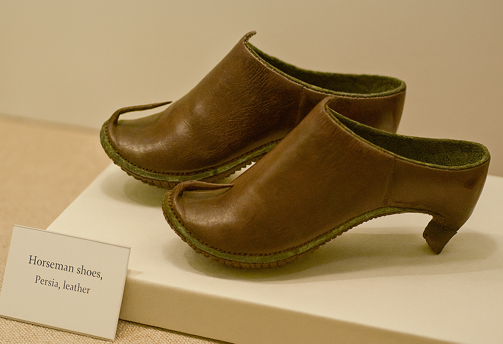 Ancient Persian horseman shoes made of leather with raised heels, displayed in a museum.