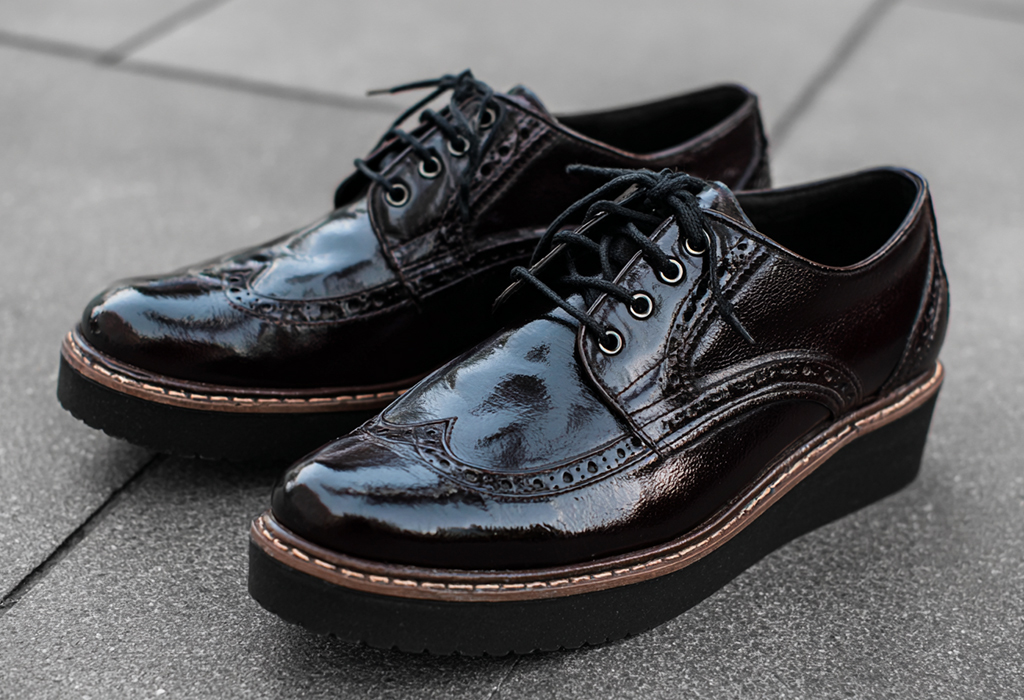 Glossy dark brown brogue shoes with wedge heels on a tiled surface