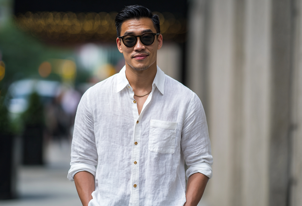 Stylish man in a white linen shirt and sunglasses walking confidently in an urban setting