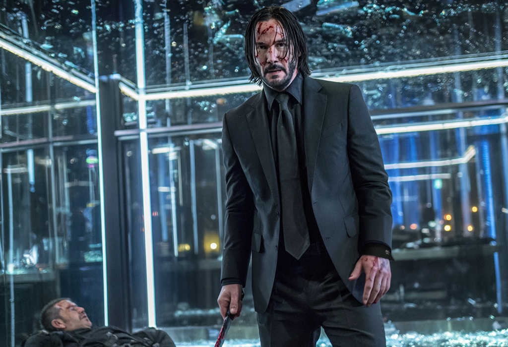 John Wick in bloodied black suit holding weapon in mirrored room after a fight scene