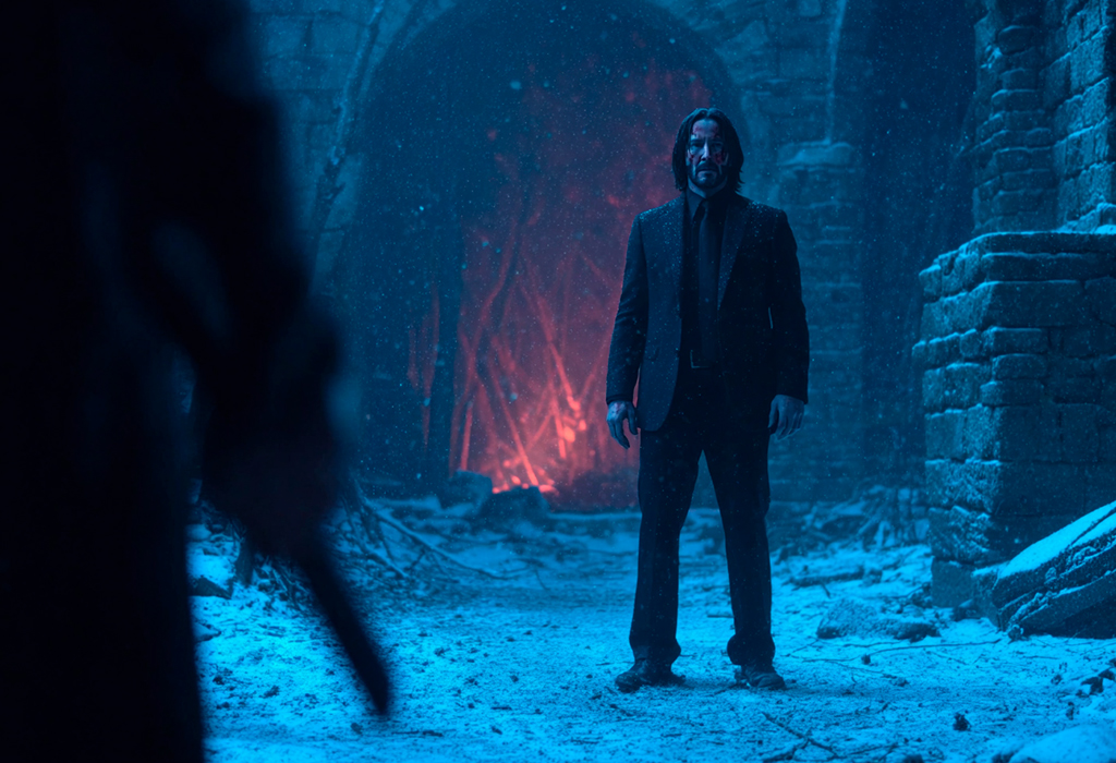 John Wick in black suit with blood on face sitting on city stairs, looking worn but alert
