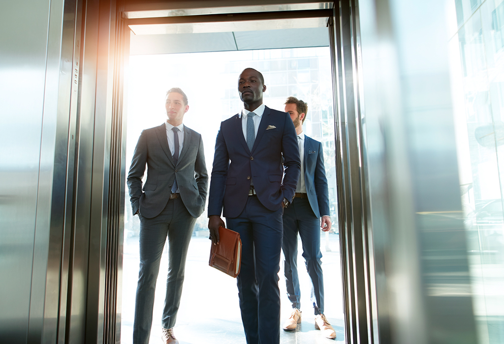 Black executive exits elevator; colleagues follow respectfully