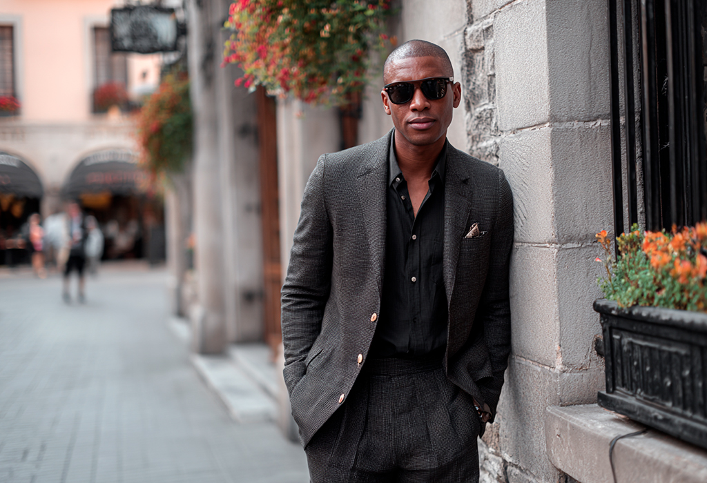 Man wearing all-black outfit leaning against stone wall