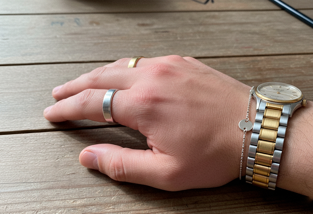 Man’s wrist showing gold wedding ring, silver band, and mixed-metal watch