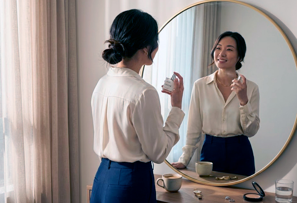 Asian woman in front of mirror spraying perfume before work, dressed elegantly for office